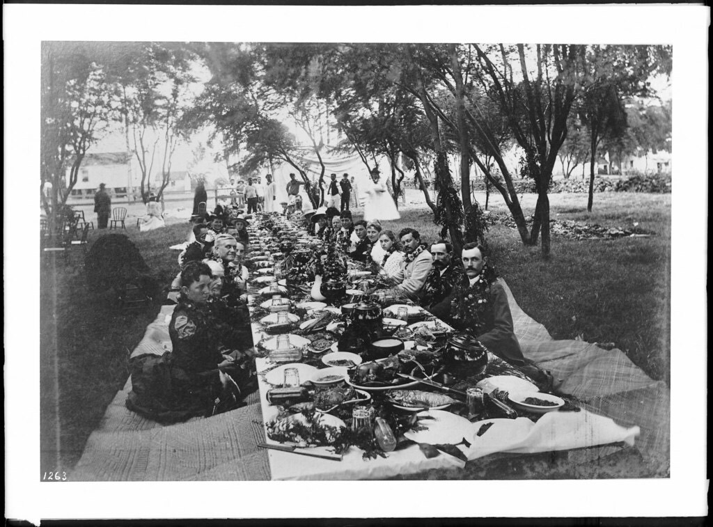 A long lūʻau table laid outdoors, photographed in the late nineteenth century
